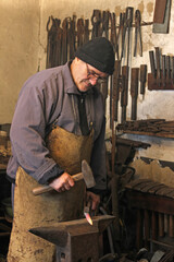 Blacksmith at work, mature man hitting a red-hot iron with a hammer on the anvil. Blacksmith forging red-hot metal bar in smithy