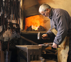 Blacksmith at work, mature man hitting a red-hot iron with a hammer on the anvil. Blacksmith forging red-hot metal bar in smithy