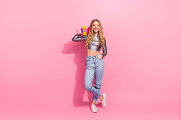 Blonde girl in shiny top holding skateboard against pink background showcasing trendy fashion and joyful vibes