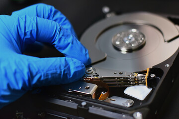 Obraz premium A technician in a hard disk assembly lab is disassembling and repairing a hard disk on a workbench, wearing gloves and holding a screwdriver to repair the hard disk or recover data.