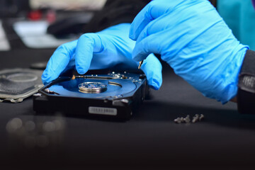 Obraz premium A technician in a hard disk assembly lab is disassembling and repairing a hard disk on a workbench, wearing gloves and holding a screwdriver to repair the hard disk or recover data.