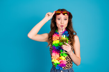 Fashionable young woman with vibrant lei holding a drink against a blue background, exuding summer...