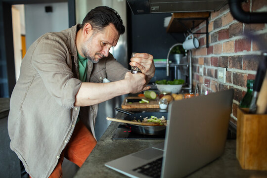 Man cooking in kitchen while watching laptop