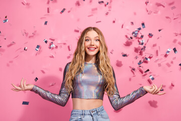 Happy young woman in vibrant outfit posing with falling confetti against pink background