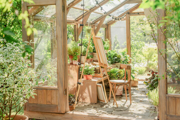 A sunlit greenhouse with an easel and flowers.