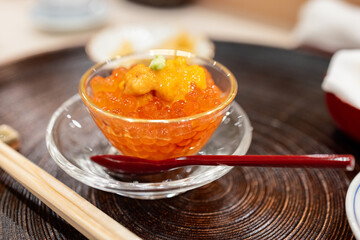 Japanese appetizer of salmon roe served in a glass bowl topped with sea urchin and wasabi presented on a wooden tray showcasing the refined flavors and aesthetics of Japanese cuisine