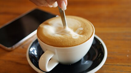 Relaxing moment of stirring invigorating cappuccino before work coffee foam swirling gently in cup Morning coffee ritual sets calm tone for day Coffee lovers enjoy peaceful start with fresh coffee