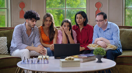 Indian family group mom dad son teen girl child watch film horror scene movie feel fear spend day time house Young adult man women sitting cozy sofa couch use laptop look screen have fun joy enjoy