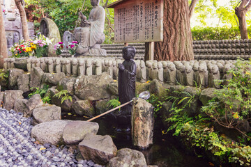 Spiritual Jizo statues at Hase temple Kamakura Japan stand near a water purification site with a dark stone figure a ritual ladle and floral offerings