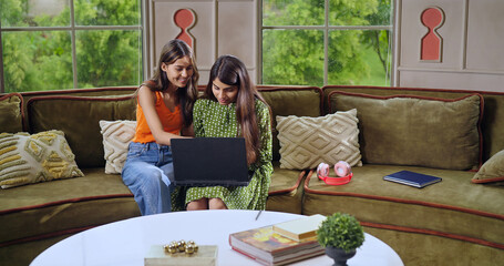 Indian happy young adult gen z woman lady sitting on cozy sofa couch use laptop look screen do work...