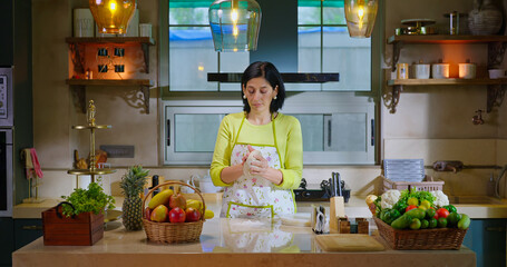 Indian asian gen x woman lady chef wear apron knead flour with hand indoor modern kitchen spend time young adult alone female mother mom bake food pastry dough bread on counter table enjoy day house