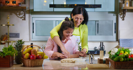 Indian happy woman lady with cute teen age cute girl rolling raw flour dough learn cooking food indoor home smiling young mom teach to kid child baking cookies enjoy day indoor modern home kitchen