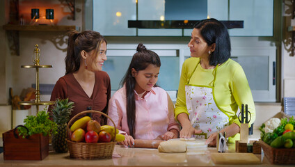Indian happy young woman lady with cute teen cute girl hold roller rolling raw flour dough learn cook food indoor home adult mom teach kid child trying to bake cookies enjoy day modern home kitchen