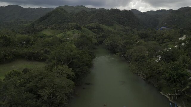 Drone lowers over Cahabon River on cloudy afternoon as group on tubes float down river in Semuc Champey