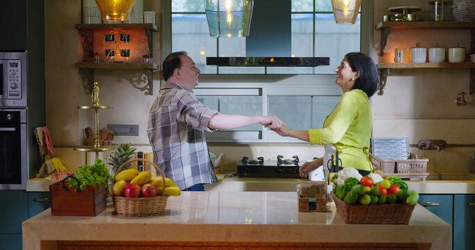 Indian Asian happy gen x lovely couple pair hold hand do casual waltz dance music feel good indoor home wife man women male female lady mom dad love care mood have fun joy enjoy spend day time - Powered by Adobe