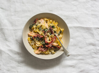 Homemade fettuccine pasta with chicken, sun-dried tomatoes and spinach in cream sauce on a light background