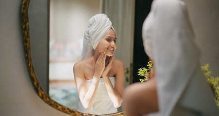 Indian young adult gen z woman lady wrapped towel on head and body look mirror apply make up cream on dry cheek face teen age girl female hold bottle take liquid hand do fresh day skin care house home