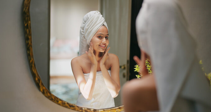 Indian young adult gen z woman lady wrapped towel on head and body look mirror apply fresh make up cream on dry cheek face teen age girl do female hand facial massage day skin care house home