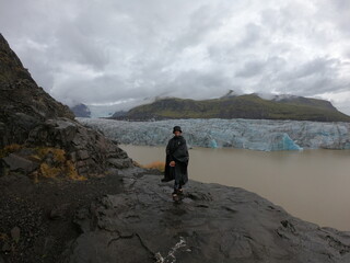 A traveler stands before the serene glacial waters of Fjallsárlón, where floating icebergs...