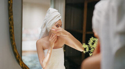 Indian young adult gen z woman lady hold blade razor do self skin care home teen age female girl wrapped towel on head body look mirror use tool shave her wet face clean upper lip cheek facial hair