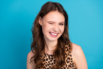 Charming Young Woman Winking in Leopard Print Top Against Vibrant Bright Blue Background, Exuding Confidence, Style, and Joy