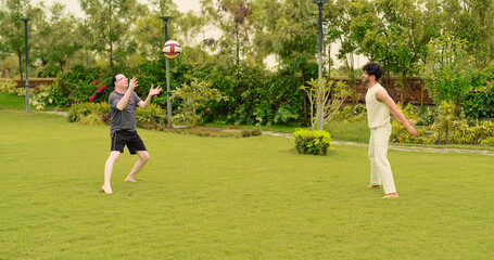 Indian happy adult playful two sporty man guys standing playing casual ball game outdoor garden park enjoy day. Middle aged elder older active male dad have fun with young son spend time have fun joy