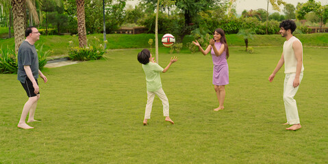 Indian happy active family group playing casual foot ball game enjoy outdoor garden park middle aged older dad spend day with cute teen child kids son young adult girl boy have fun joy sports time	