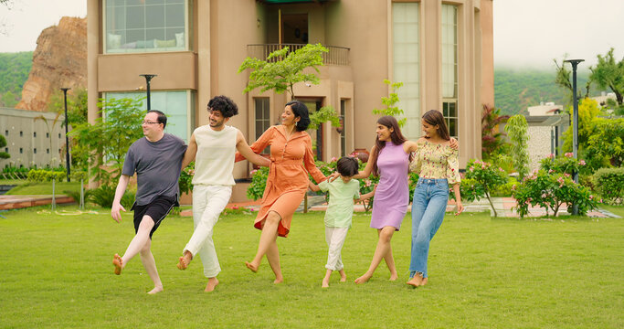 Indian happy family group dancing with teen girl child cute son kid boy enjoy day outdoor home park. Adult mom dad man woman young male female have fun joy play game spend time at outside garden house