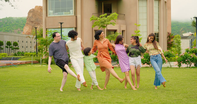 Indian happy family group dancing with teen girl child cute son kid boy enjoy day outdoor home park. Adult mom dad man woman young male female have fun joy play game spend time at outside garden house