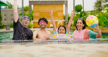 Indian happy family group with teen child dancing look cam enjoy outdoor resort pool edge trip mom dad young adult girl boy make female do pose have fun joy spend day time at outside water park