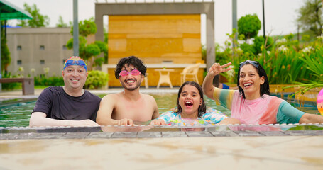 Indian happy family group with teen child dancing look cam enjoy outdoor resort pool edge trip mom dad young adult girl boy make female do pose have fun joy spend day time at outside water park