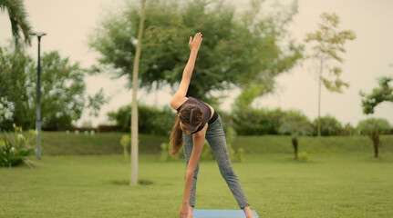Indian young adult gen z sporty woman lady do self health care warm up on mat in fresh air park...