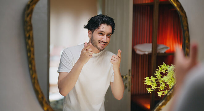 Indian Asian gen z young adult single happy man male guy smiling look mirror touch beard daily care routine feel proud good ready for new Joyful day enjoy indoor house
