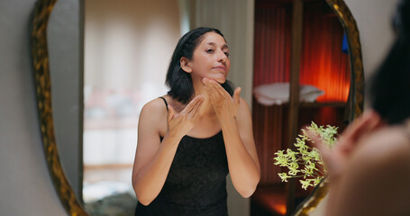 Indian gen x senior mature adult older elder short hair woman lady look mirror use beauty apply soft cream on dry face female mom do hand massage fresh day skin care at house home