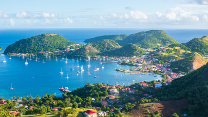 Vue de haut de la baie des Saintes en Guadeloupe avec la mer des Caraïbes, l'île de Terre de Haut, et des bateaux par une journée ensoleillée avec des nuages.