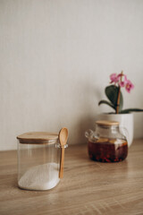 Glass teapot with berry tea on a wooden table, next to a blooming orchid in a ceramic pot.