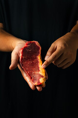 A hand pointing at the yellowish fat on a raw steak, with a dark background