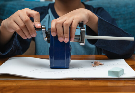 A child manually turning the handle of mechanical pencil sharpener