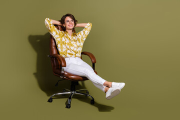 Confident young businesswoman with brunette hair relaxes in an elegant office chair against a khaki...