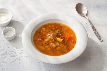 Homemade vegetable soup with pumpkin, bell pepper, tomato, and buckwheat on a light grey table. Delicious vegan comfort food
