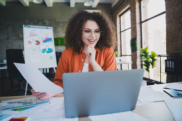 Young woman with curly hair working professionally on laptop in a brightly lit modern office...