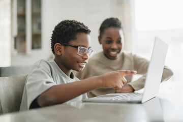 Little American boy studying online with laptop in kitchen with sister © Louis-Paul Photo