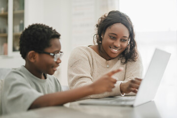 Little American boy studying online with laptop in kitchen with mother © Louis-Paul Photo