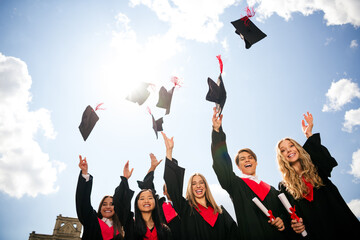 Group of happy young graduates in caps and gowns celebrating outdoors on a sunny day
