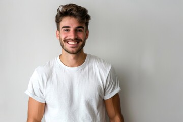 Fototapeta premium Portrait of a handsome young man in white t shirt smiling while standing against white background