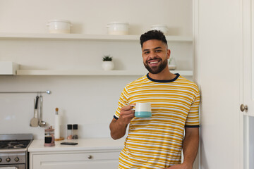 Smiling man in kitchen holding coffee mug, enjoying morning at home, copy space
