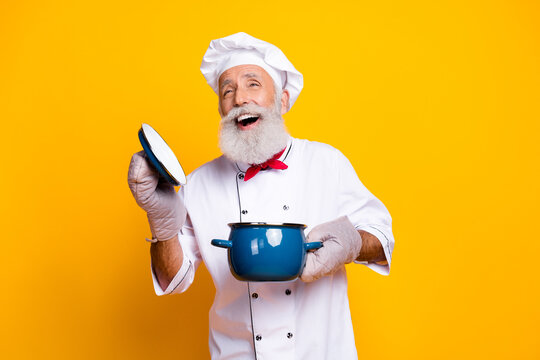 Joyful senior chef holding a cooking pot against a yellow backdrop, celebrating culinary skills and a passion for cooking