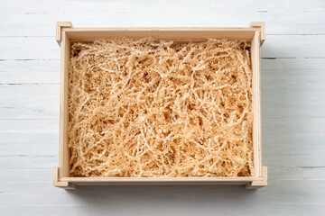 Empty wooden gift box with natural shredded crinkle-cut paper filler on light blue wooden background