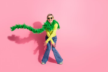 Cheerful young woman in vibrant outfit posing against a pink background with a fun green boa creating a lively and trendy scene