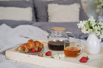 Wooden tray with tea, croissant and strawberries on the bed in the bedroom. Breakfast in bed